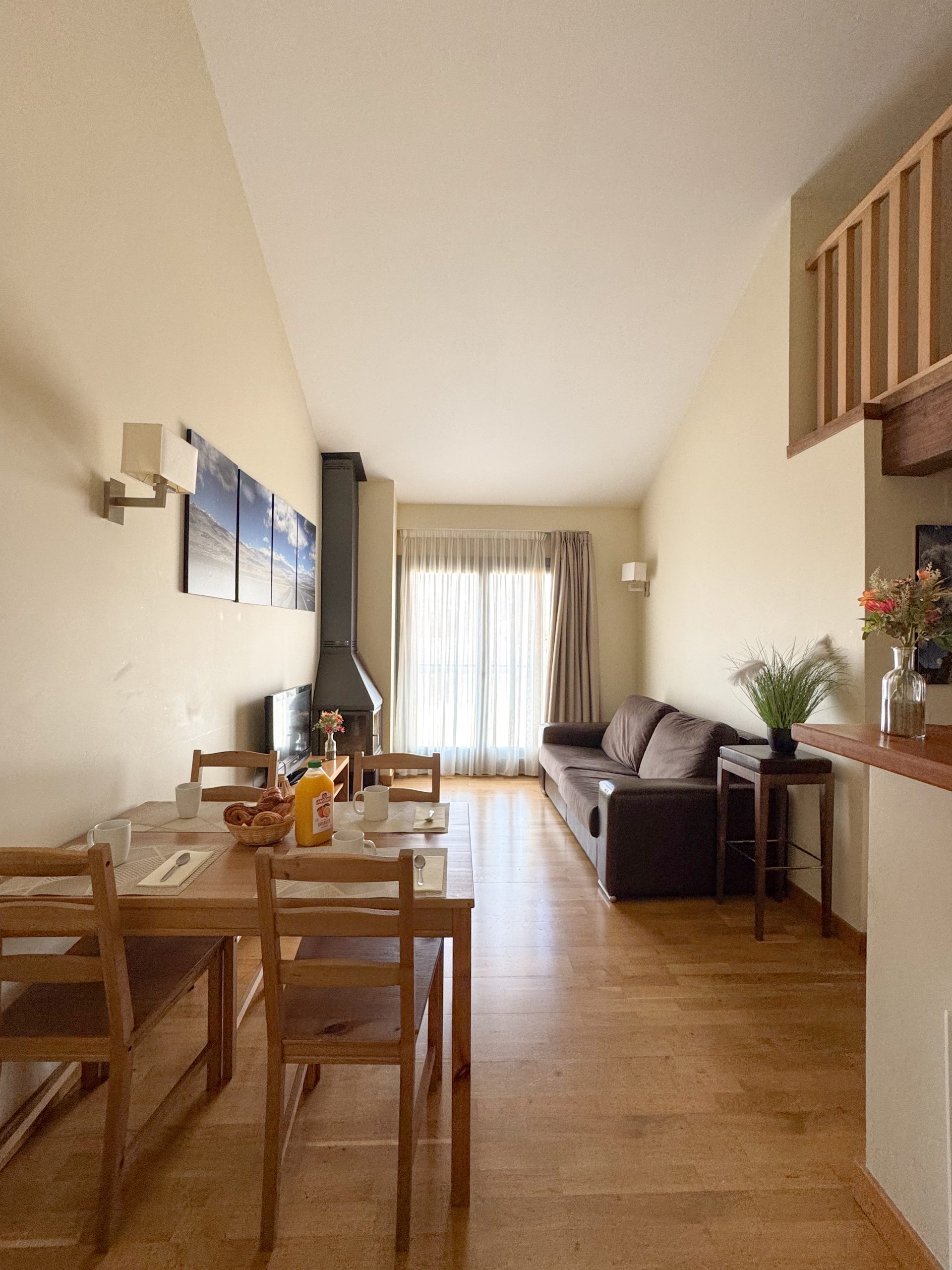 Salon en duplex avec canapé, table à manger en bois pour 4 personnes, poêle à bois et balcon lumineux à l’Appart'hôtel Cerdanya.